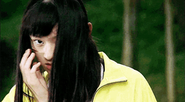 a girl with long black hair and a yellow jacket is covering her face with her hair