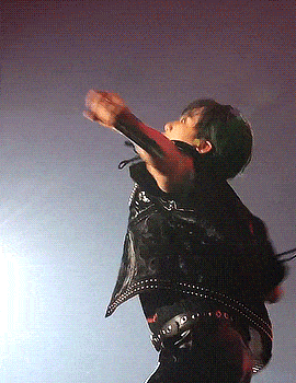 a man wearing a black vest with studs on it is dancing on a stage