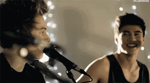 a man is singing into a microphone while another man plays the guitar .