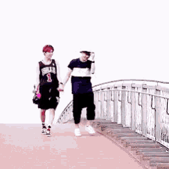 two young men are walking across a bridge holding hands .