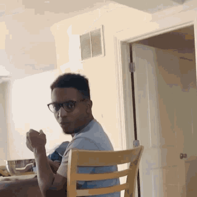 a man wearing glasses is sitting in a chair in front of a door .