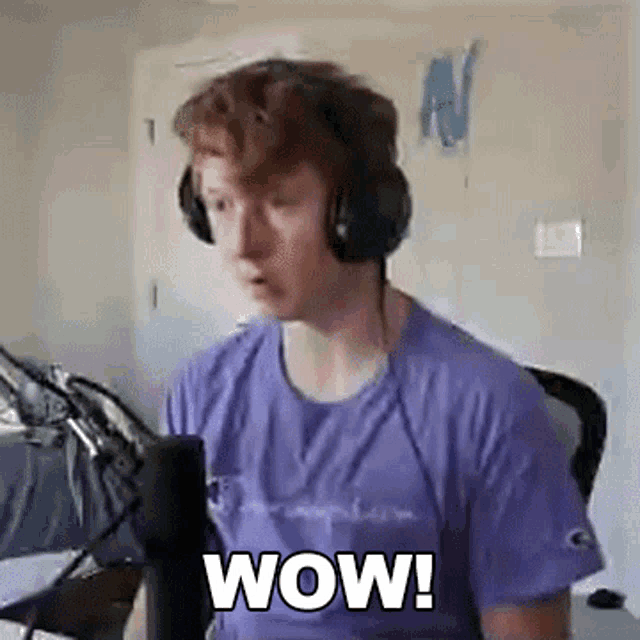 a young man wearing headphones and a purple shirt is sitting in front of a microphone and saying wow .