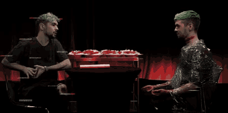 two men with green hair are sitting at a table with cupcakes on it