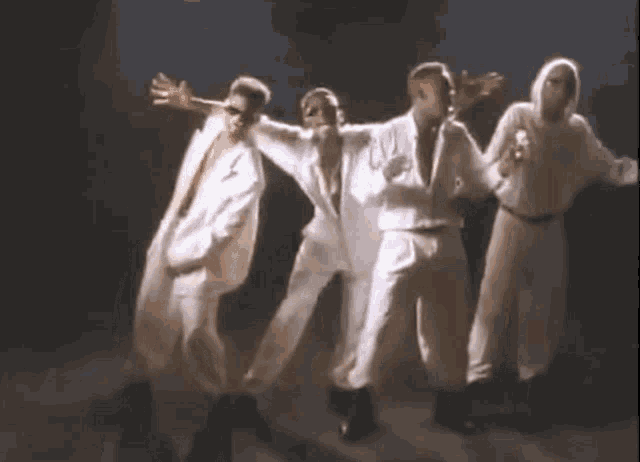 a group of men in white suits are dancing together on a stage in a dark room .