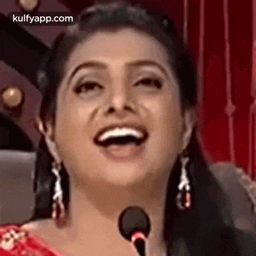a woman is laughing in front of a microphone while wearing earrings .