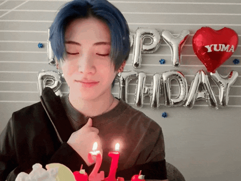 a young man blows out a birthday candle in front of a happy birthday banner