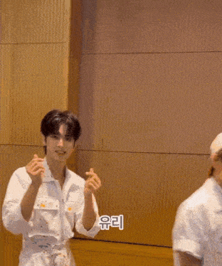 a man in a white shirt is covering his mouth with his hand while sitting in front of a wall .