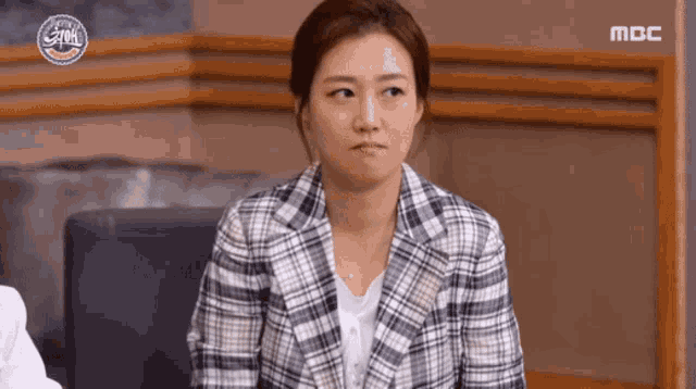 a woman in a plaid jacket is sitting in front of a sign that says mbc