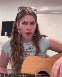 a woman playing a guitar with a shirt that says petite