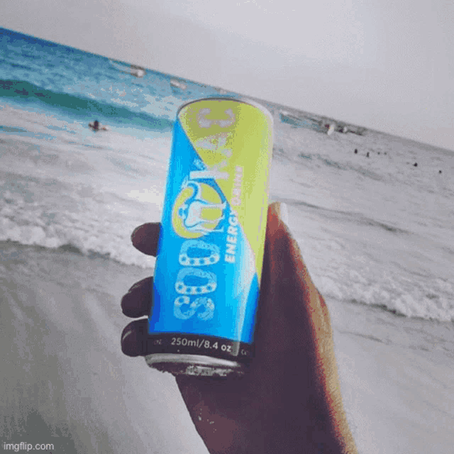 someone is holding a can of energy drink in front of a beach