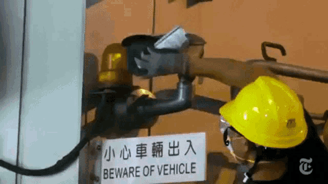 a person wearing a yellow hard hat is working on a beware of vehicle sign