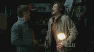 two men are standing next to each other and one has a light in his hand and the other has a cw logo on his shirt