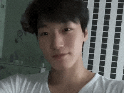 a young man is taking a selfie in front of a tiled wall while wearing a white shirt .