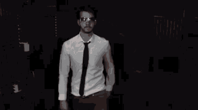a man in a white shirt and tie is holding a pair of sunglasses in his mouth .