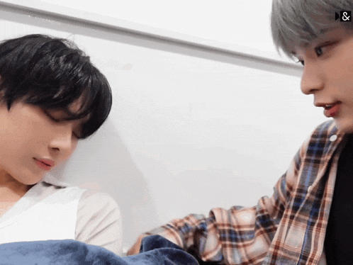 a man in a plaid shirt talks to another man who is laying down
