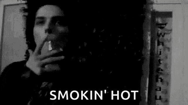 a black and white photo of a man smoking a cigarette and the words `` smokin ' hot '' .