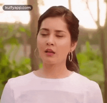 a woman wearing hoop earrings and a white shirt is making a funny face with her eyes closed .