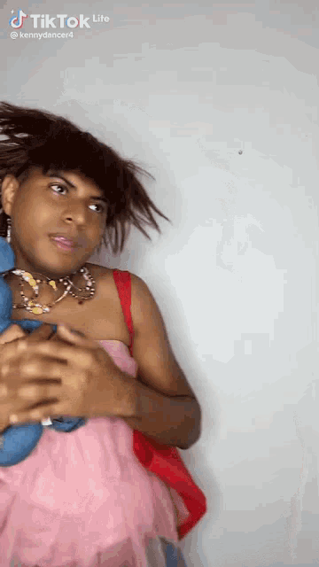 a woman in a pink dress is holding a stuffed animal and has a tiktok lite sticker on her face