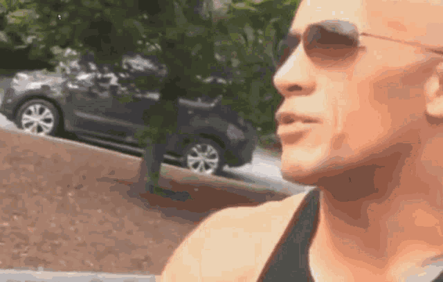 a man wearing sunglasses is standing in front of a car on a hill