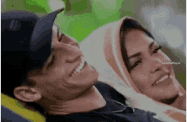 a man and a woman are sitting next to each other and smiling . the woman is wearing a hijab .