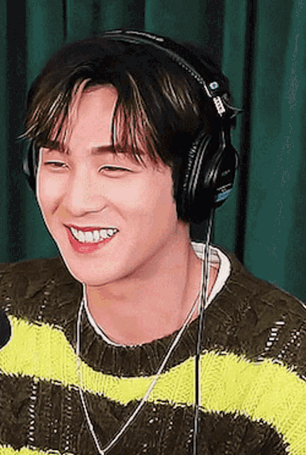 a young man wearing headphones and a sweater smiles