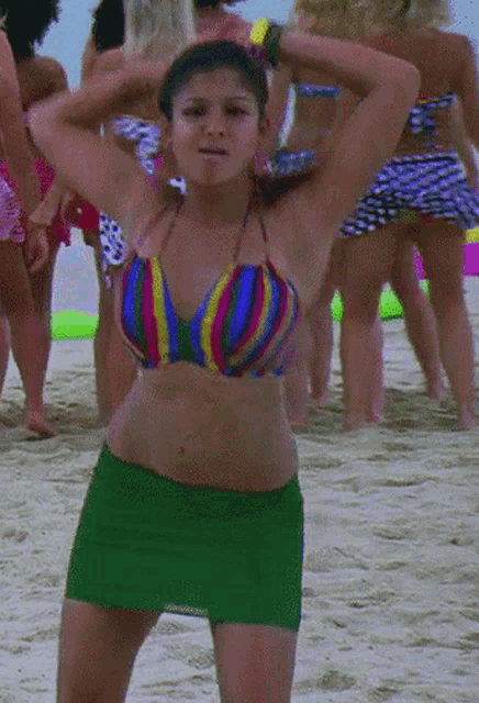 a woman in a bikini and green skirt dancing on the beach