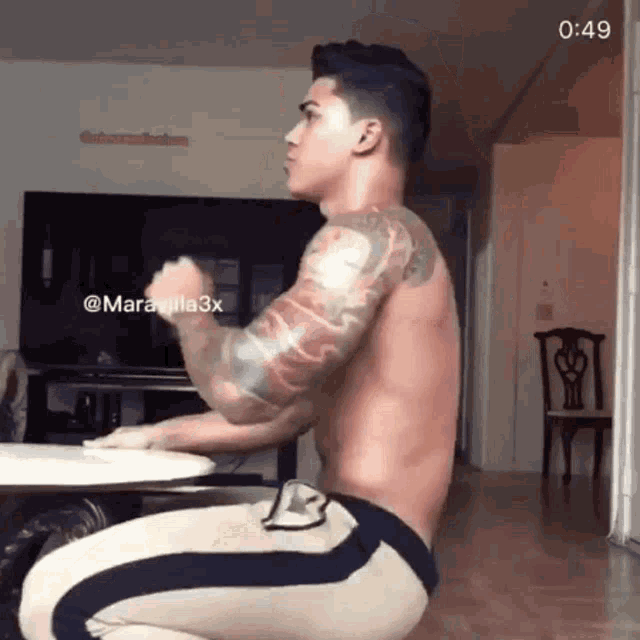 a shirtless man is squatting down in front of a television while wearing shorts with the letter b on the side