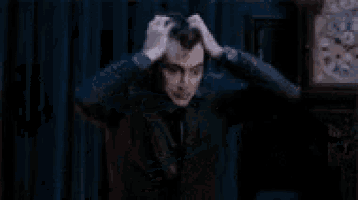 a man is sitting in front of a clock with his hands on his head and a clock in the background .