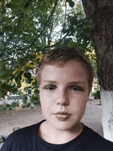 a young boy with makeup on his face stands next to a tree