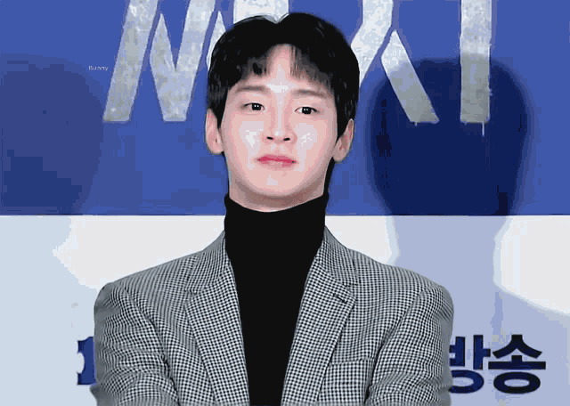 a young man in a suit and turtleneck stands in front of a sign that says ' bunny ' on it