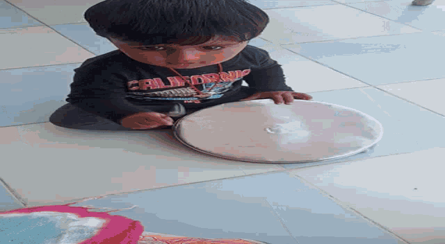 a young boy wearing a california shirt sits on the floor holding a pot