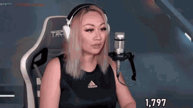 a woman wearing headphones and a black adidas shirt is sitting in front of a microphone