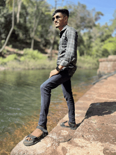 a man wearing sunglasses leans on a rock near a body of water