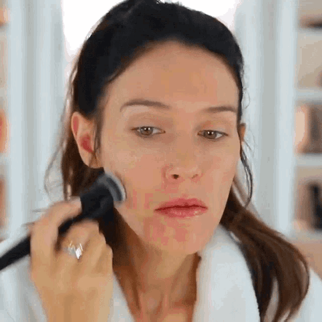 a woman in a white robe is applying makeup to her face