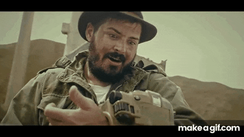 a man with a beard and a hat is holding a camera in his hand .
