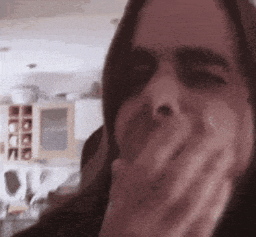 a woman with long hair is covering her mouth with her hand in a kitchen .