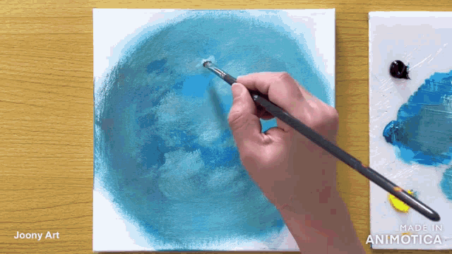 a person is painting a blue circle on a canvas with a brush