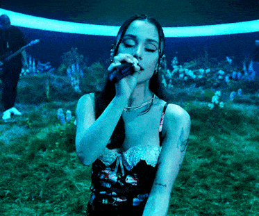 a woman is singing into a microphone in a field