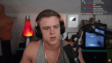 a man wearing headphones and a gold chain stands in front of a microphone on a twitch stream