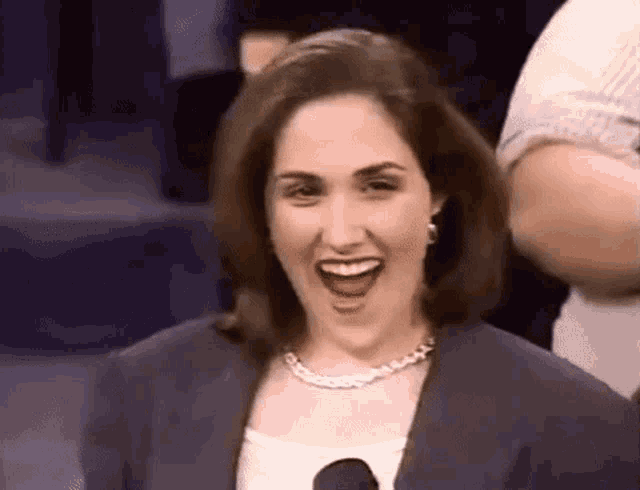 a woman is smiling with her mouth open and wearing a necklace and a jacket .
