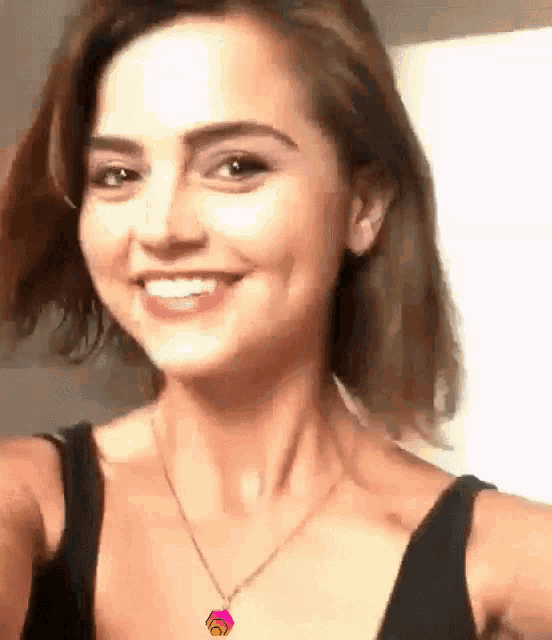 a woman wearing a black tank top and a necklace is smiling for the camera .