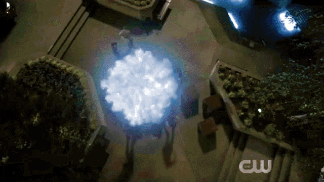 a group of people standing around a glowing object with a cw logo in the corner