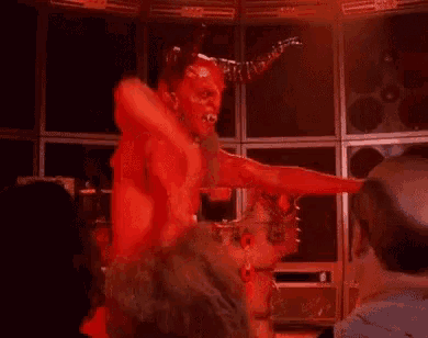 a man dressed as a devil with horns is dancing in front of a group of people in a dark room .