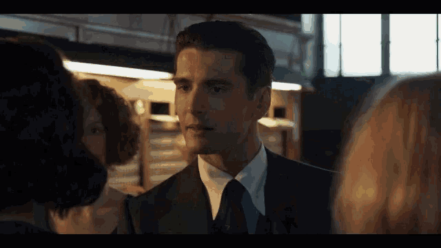 a man in a suit and tie is talking to a group of women .