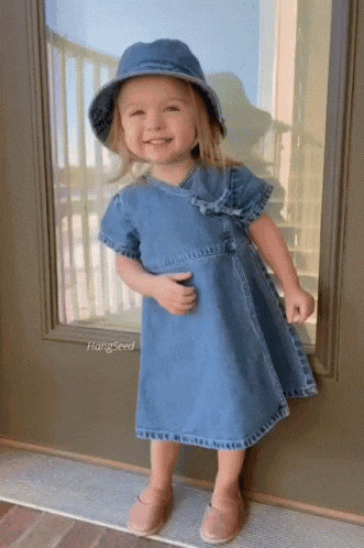 a little girl wearing a denim dress and hat is standing in front of a door that says hangseed on it