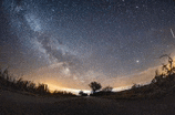 a milky way galaxy is visible in the night sky above a field .