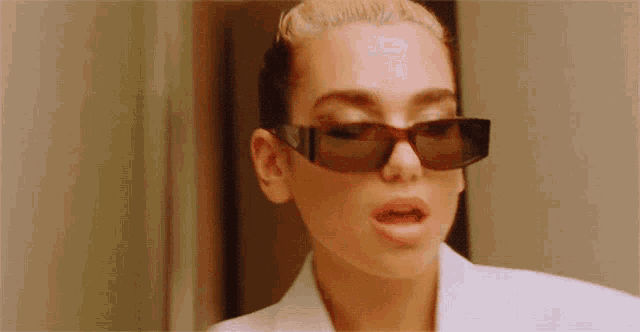 a woman wearing sunglasses is looking at herself in the mirror .