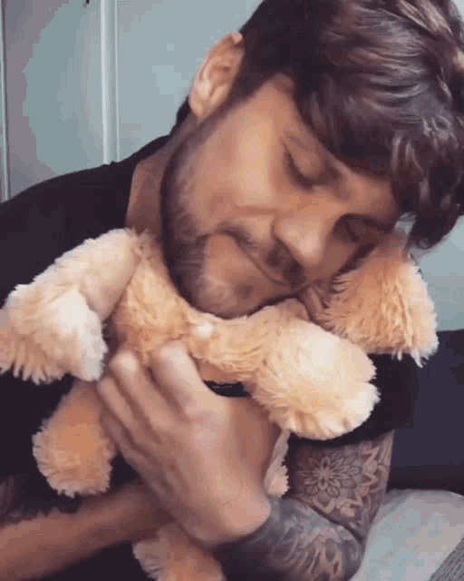 a man with a tattoo on his arm is hugging a stuffed animal