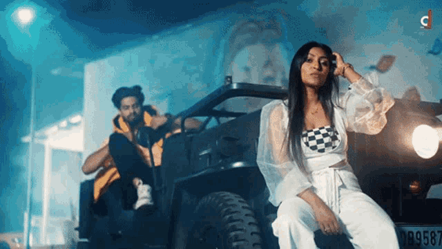 a man sits on the back of a jeep next to a woman who is sitting on the front of the vehicle