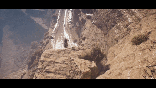 a man is riding a bike on a rocky cliff near a waterfall
